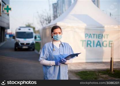 Portrait of serious female key front line worker in blue PPE uniform,standing outside EMS hospital or ICU clinic facility entrance,UK COVID-19 drive through testing site,rt-PCR Coronavirus diagnostic