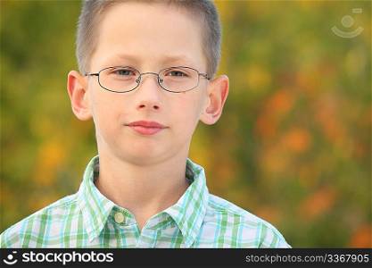 portrait of serious little boy with glasses in early fall park.
