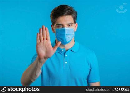 Portrait of serious man in professional medical mask showing rejecting gesture by stop palm sign. Guy isolated on blue background. Portrait of serious man in professional medical mask showing rejecting gesture by stop palm sign. Guy isolated on blue background.