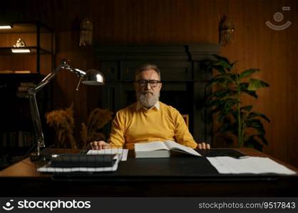 Portrait of serious pensive senior man on retirement working at home office in evening. Elderly male sitting at table taking break while reading book at library. Portrait of serious pensive senior man on retirement working at home office