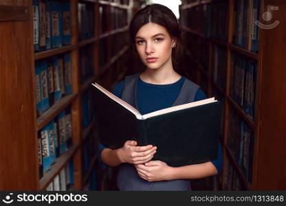 Portrait of serious student with open book reading it in college library.. Student with open book in college library.