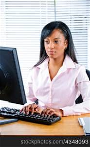 Portrait of serious young black business woman at desk typing on computer