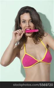portrait of sexy brunette lady in summertime wearing colorful bikini and eating popsicle
