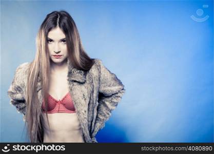 Portrait of sexy girl with long hair. Young woman in red bra underwear and fur coat on blue. Femininity. Studio shot.