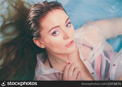 Portrait of sexy seductive woman floating in swimming pool water. Pretty alluring young girl wearing wet white shirt. Top view.. Portrait of sexy seductive woman in water.