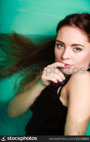 Portrait of sexy seductive woman wearing black dress in swimming pool water. Young attractive alluring girl floating. Top view.. Portrait of sexy seductive woman in water.