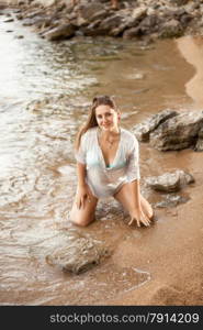 Portrait of sexy woman in shirt kneeling on sandy beach