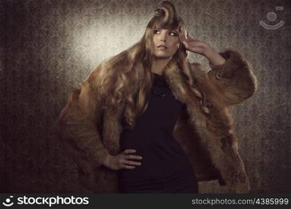 portrait of sexy young blonde woman in fashion pose with creative hair-style and elegant winter style. Wearing cute fur and black dress on grunge color