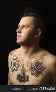 Portrait of shirtless Caucasian man with tattoos and mohawk against black background.
