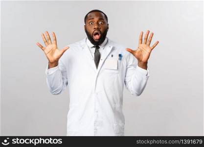Portrait of shocked and nervous african-american male doctor raising hands in surrender, trying calm down tensed family of patient, look insecure and unaware what do, stand grey background.. Portrait of shocked and nervous african-american male doctor raising hands in surrender, trying calm down tensed family of patient, look insecure and unaware what do, stand grey background