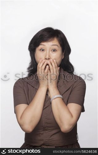 Portrait of shocked and surprised woman with hands covering her mouth, studio shot