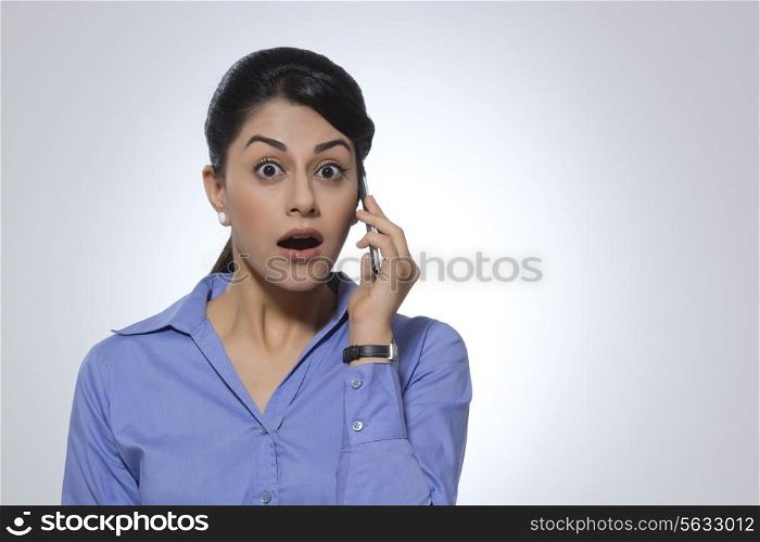 Portrait of shocked businesswoman using mobile phone against gray background