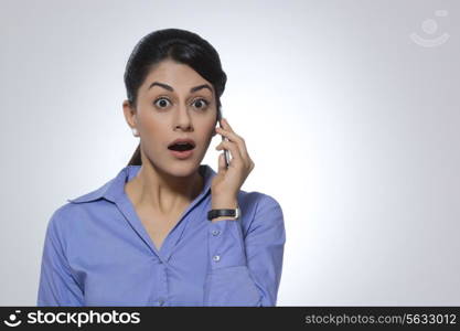 Portrait of shocked businesswoman using mobile phone against gray background