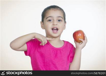 Portrait of shocked girl showing fresh apple against colored background