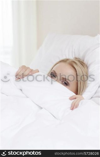 Portrait of shy young woman hiding under bedsheet
