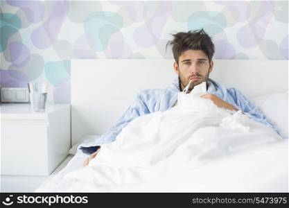 Portrait of sick man with thermometer in mouth reclining on bed at home