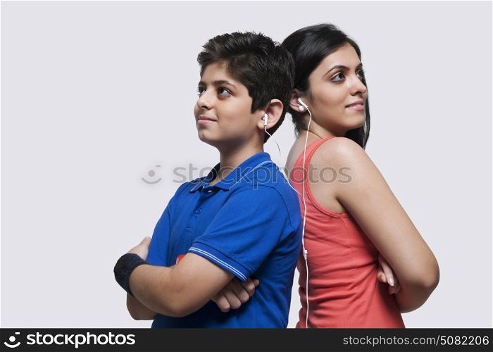 Portrait of sister and brother standing back to back and listening music