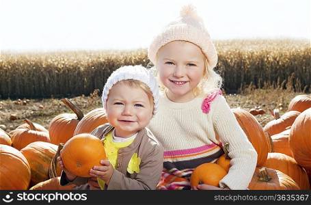 Portrait of sisters with pumpkin sitting on farm