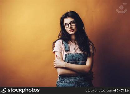 Portrait of smart beautiful brunette girl in eyeglasses with natural make-up, on yellow background.. Portrait of smart beautiful brunette girl in eyeglasses with natural make-up, on yellow background
