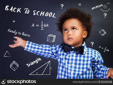 Portrait of smart curly African American schoolboy in the school on mathematics lesson, solving task near blackboard