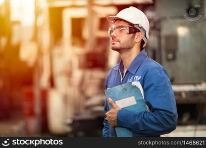 Portrait of smart engineer education machine service manual book happy worker standing proudly in heavy industry background.