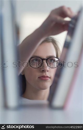 portrait of smart looking famale student girl in collage school library, selecting book to read from bookshelf