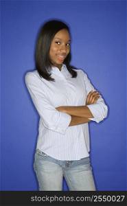 Portrait of smiling African-American teen girl with crossed arms standing in front of blue background.