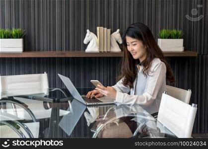 Portrait of smiling asian beautiful young businesswoman sitting at workplace with using the smart mobile phone, Business lifestyle and technology concept