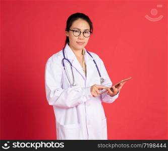 Portrait of smiling beautiful asian young woman doctor with digital tablet isolated on red background