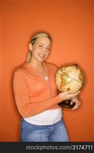 Portrait of smiling blond Caucasian teen girl holding globe standing against orange background.