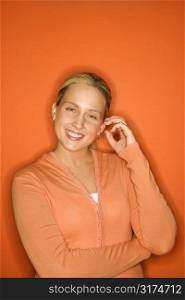 Portrait of smiling blond Caucasian teen girl standing against orange background.
