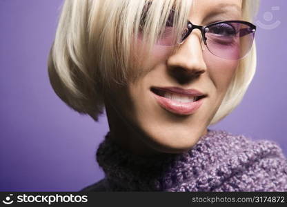 Portrait of smiling blond young adult Caucasian woman on purple background wearing sunglasses and scarf.