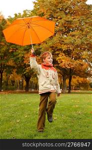 Portrait of smiling boy in autumn park. In hand umbrella, looks aside.