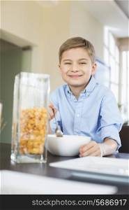 Portrait of smiling boy pouring corn flakes in bowl at home