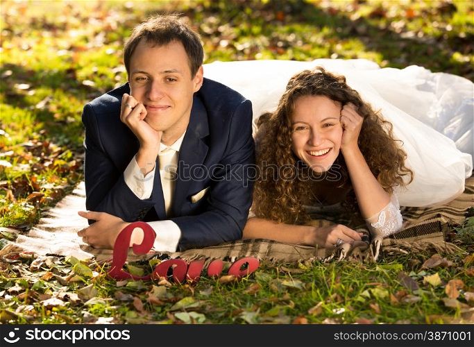 Portrait of smiling bride and groom lying on grass at autumn park