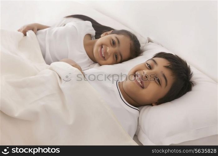 Portrait of smiling brother and sister sleeping in bed