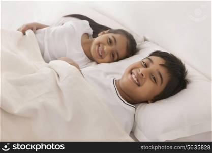 Portrait of smiling brother and sister sleeping in bed