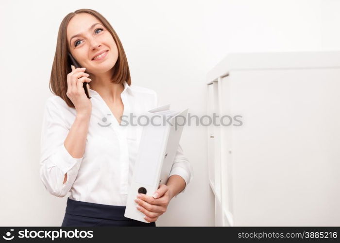 Portrait of smiling brunette businesswoman phoning while standing with a folder in office