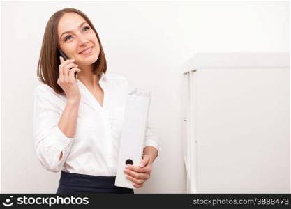 Portrait of smiling brunette businesswoman phoning while standing with a folder in office