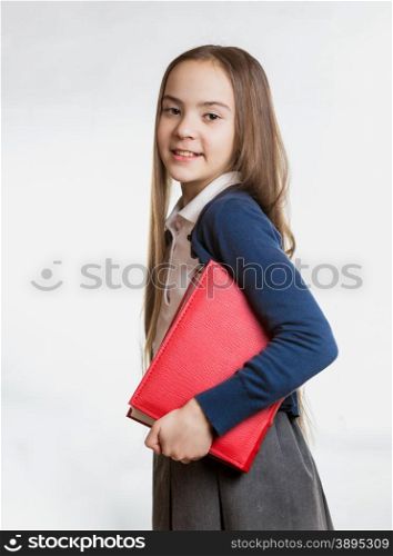Portrait of smiling brunette schoolgirl holding big red book