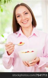 Portrait of smiling brunette woman holding a bowl with corn flakes with berries in her hands