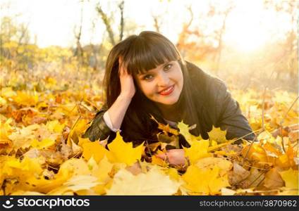 Portrait of smiling brunette woman lying on yellow leaves at autumn park