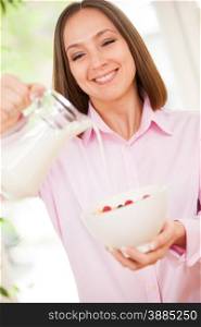Portrait of smiling brunette woman pouring a milk in corn flakes