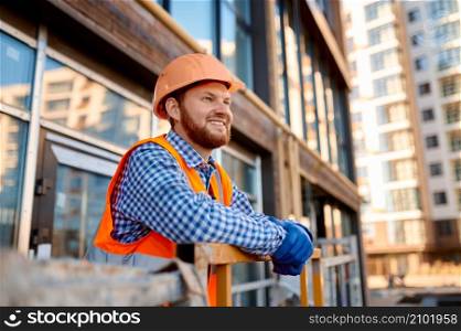 Portrait of smiling builder in helmet standing and rest on hanging cradle aerial access platform. Portrait of smiling builder on hanging cradle