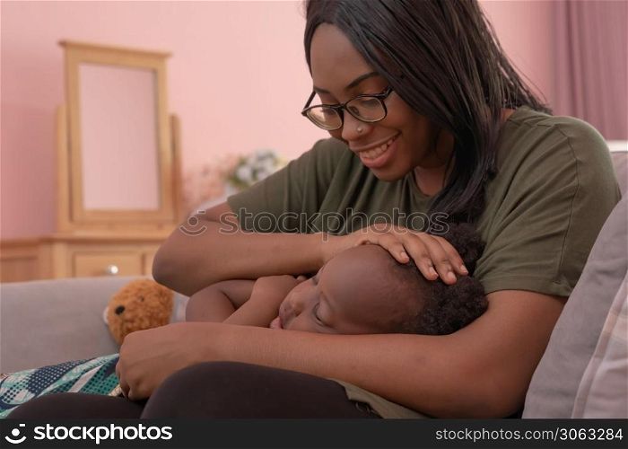 Portrait of smiling business black African american woman, a mom with her daughter lull the child to sleep at home in family relationship concept in pink bedroom. A black kid toddler girl.