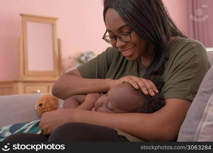 Portrait of smiling business black African american woman, a mom with her daughter lull the child to sleep at home in family relationship concept in pink bedroom. A black kid toddler girl.