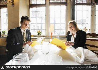 Portrait of smiling business couple with menus at restaurant table