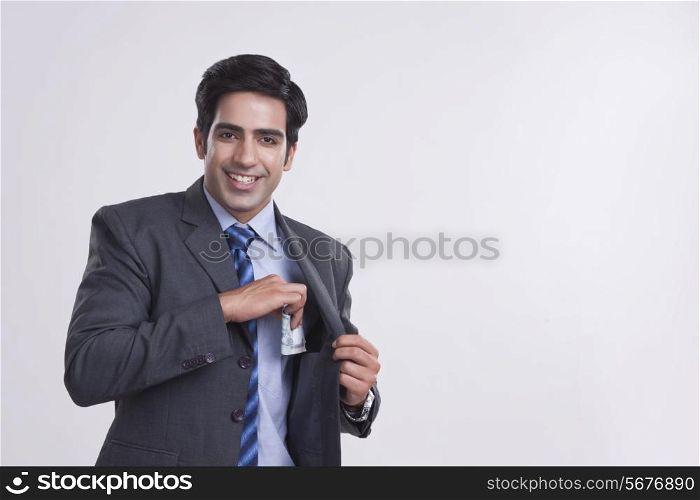 Portrait of smiling businessman keeping money in pocket over gray background
