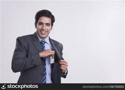 Portrait of smiling businessman keeping money in pocket over gray background