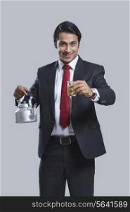 Portrait of smiling businessman offering tea over gray background